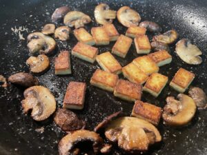 Mushrooms and Tofu sautéing in a cast iron pan