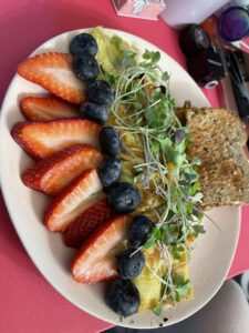 Omlette topped with microgreens. Strawberries with blueberries surround one edge of the omlette and at the top is a clice of toast.